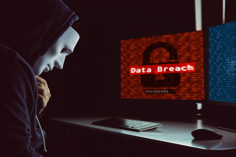 Masked hacker under hood using computer to commit data breach